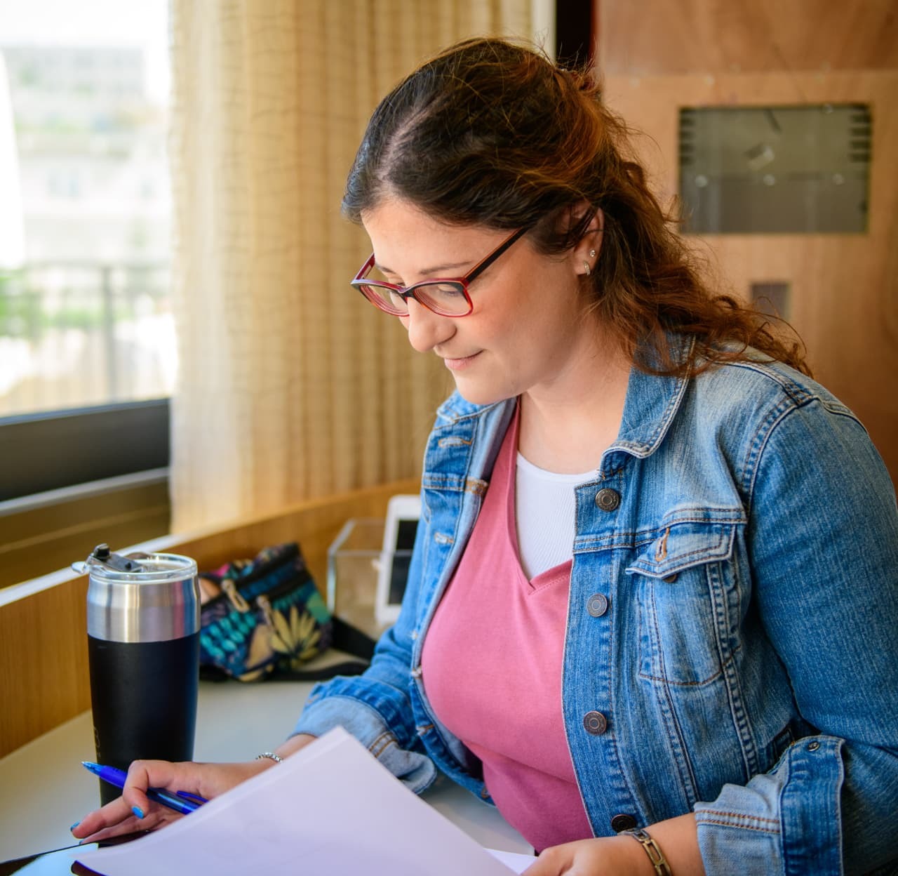A woman with glasses reading through a stack of papers at a table
